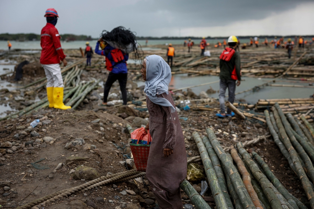 272156-1 Pasijah walks past workers constructing a toll road in Bedono village, Demak regency, Central Java Province, Indonesia, February 19, 2025. — Reuters pic
