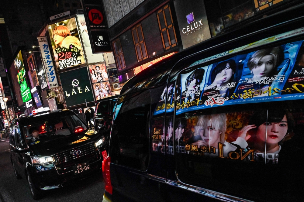 272335 This photo taken on March 31, 2025 shows advertisements for entertainment clubs reflected in the window of a passing car, along a street in the red-light entertainment area of Kabukicho in the Shinjuku district of Tokyo. — AFP pic