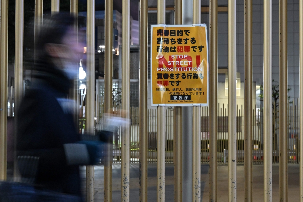 272336 This photo taken on March 31, 2025 shows a pedestrian walking past a police notice warning about street prostitution outside Okubo Park, in the red-light entertainment area of Kabukicho in the Shinjuku district of Tokyo. — AFP pic