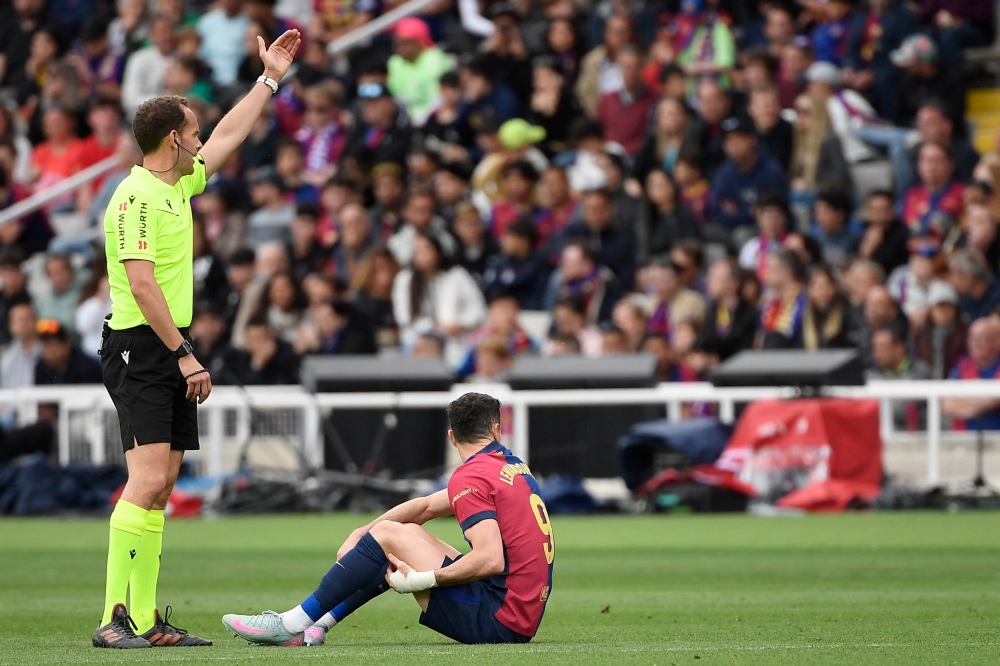 Spanish referee Melero Lopez gestures as Barcelona's Polish forward #09 Robert Lewandowski sits on the field after resulting injured during the Spanish league football match between FC Barcelona and RC Celta de Vigo at the Estadi Olimpic Lluis Companys in Barcelona April 19, 2025. — AFP pic